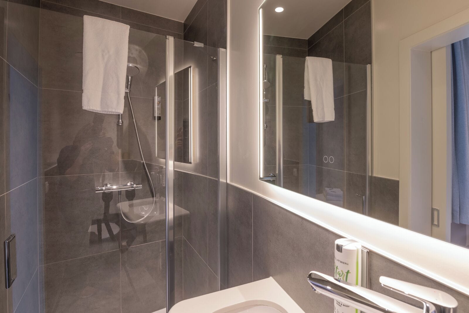 Une salle de bain moderne avec une douche à parois de verre, un grand miroir et un lavabo blanc.