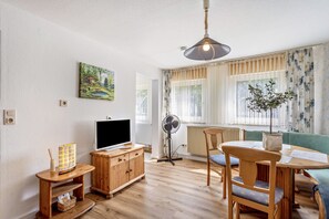Sala de estar com televisão de tela plana, móveis de madeira, um ventilador e uma janela com cortinas.