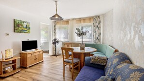 A living room with a wooden TV stand, a blue sofa, a dining table with chairs, and a painting on the wall. - Apartment '2 Bergblick, 60sqm' with Mountain View, Shared Garden and Wi-Fi (Lennestadt)