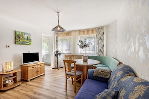 Una sala de estar con un mueble de televisión de madera, un sofá azul, una mesa de comedor con sillas y un cuadro en la pared.