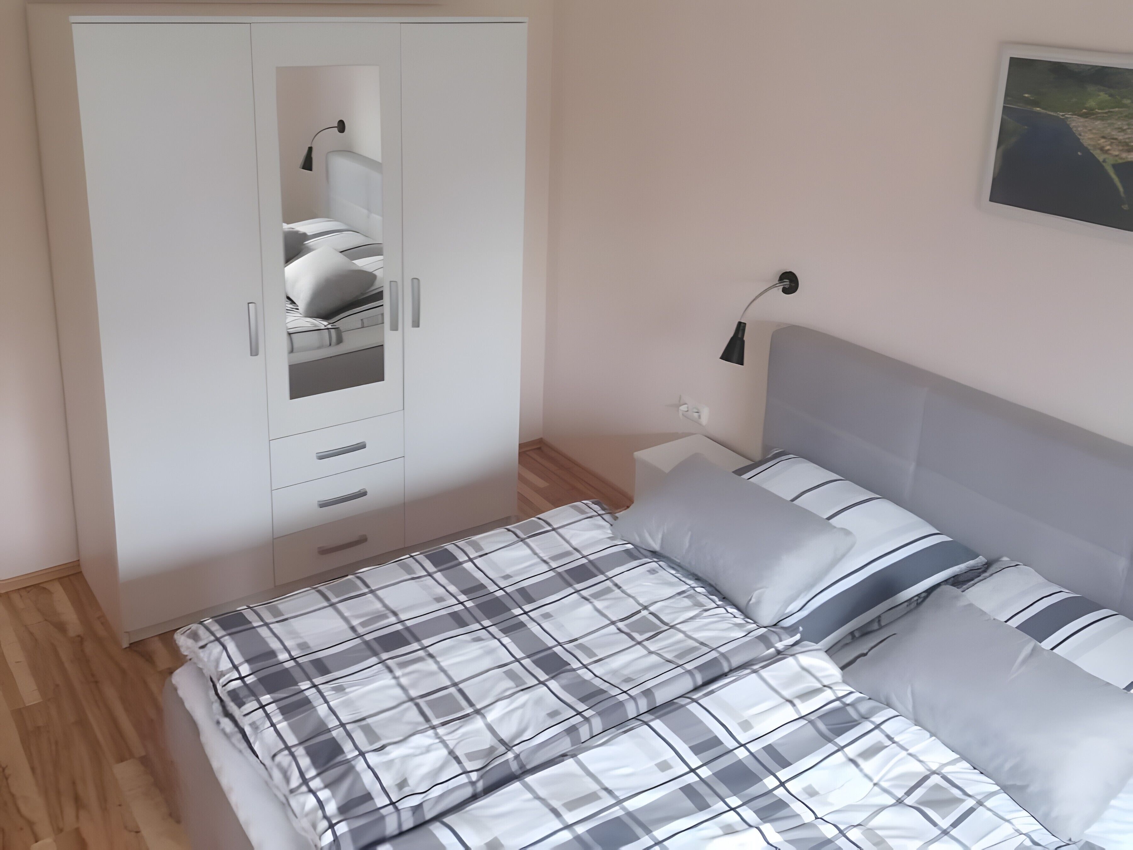 Un dormitorio con cama, armario, mesita de noche y lámpara de pared.
