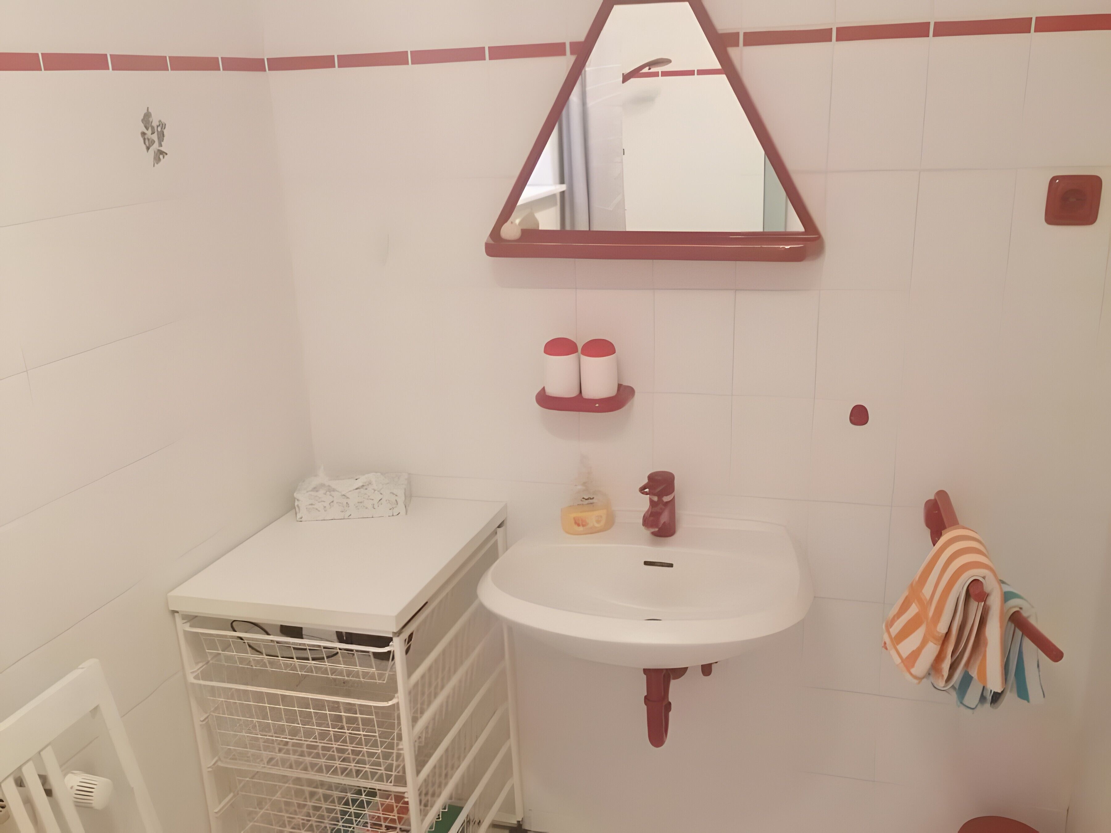 Ein Badezimmer mit einem weißen Waschbecken, einem Spiegel, einem Handtuchhalter und einem Stauraum.