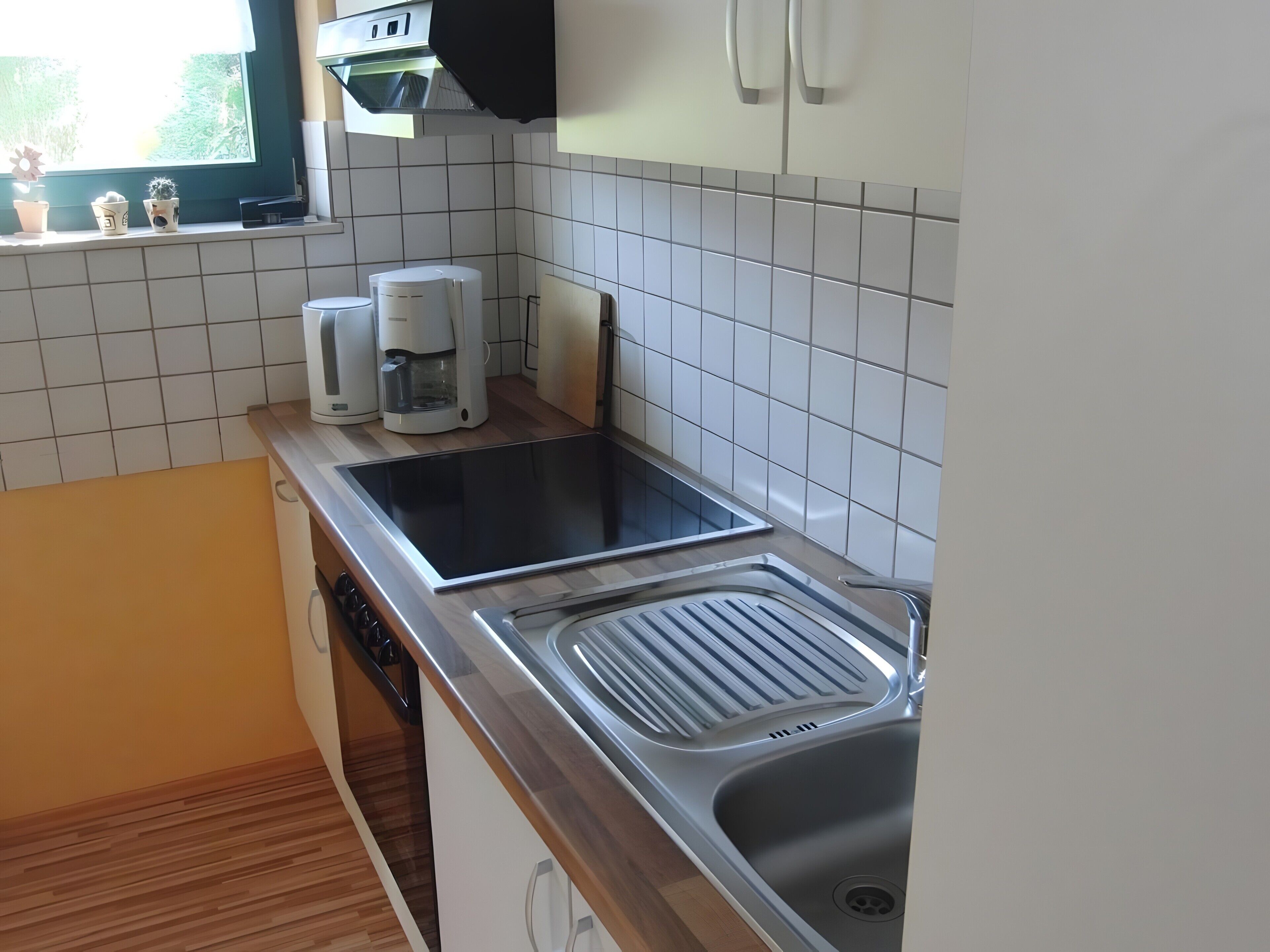 Une cuisine équipée d’une cuisinière intégrée, d’un évier et d’une fenêtre agrémentée de plantes en pot.