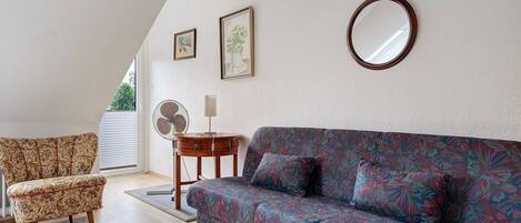 A room with a sofa, a chair, a round mirror, and two framed pictures on the wall.