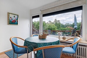 Un espace repas comprenant une table, des chaises et donnant sur un paysage verdoyant.