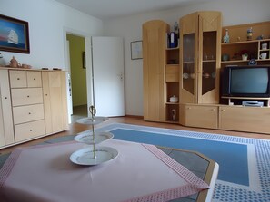 A living room with a television, wooden cabinets, a dining table with a white tablecloth, and a patterned rug. - Apartment 'Drescher' with Shared Garden, Balcony and Wi-Fi (Cuxhaven)