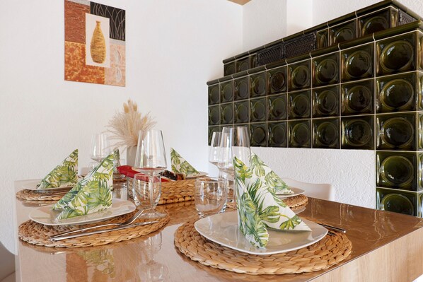 Une table à manger dressée avec des assiettes, des couverts et des verres, et un mur de bouteilles de vin en arrière-plan.