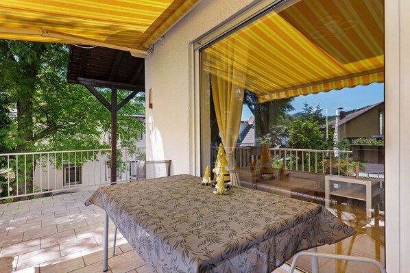 Un espacio al aire libre techado con mesa y sillas, un toldo amarillo y una puerta de cristal que da a un balcón.