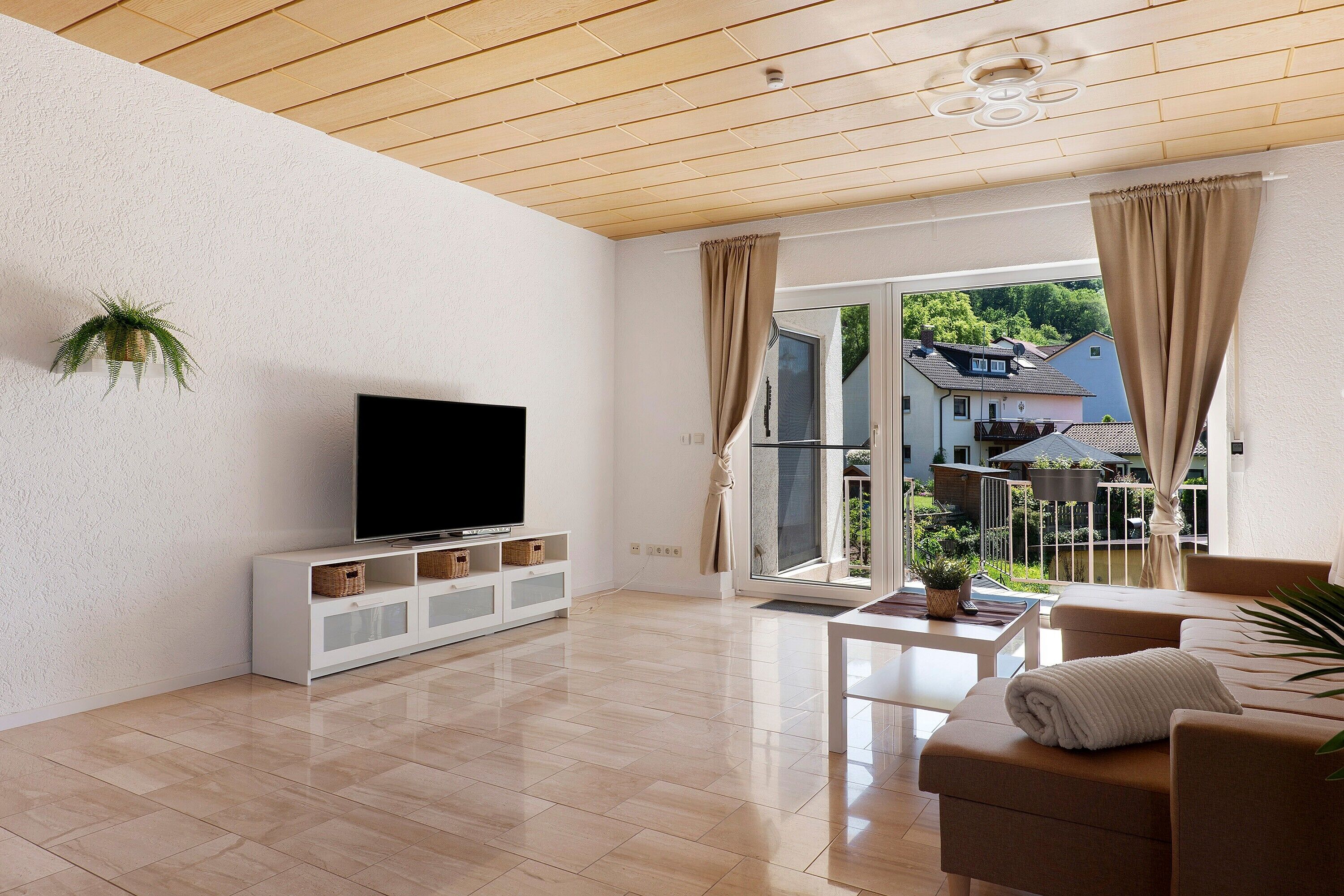 Una sala de estar moderna con una televisión de pantalla plana, un sofá, una mesa de centro y un ventanal corredero que da a un balcón.
