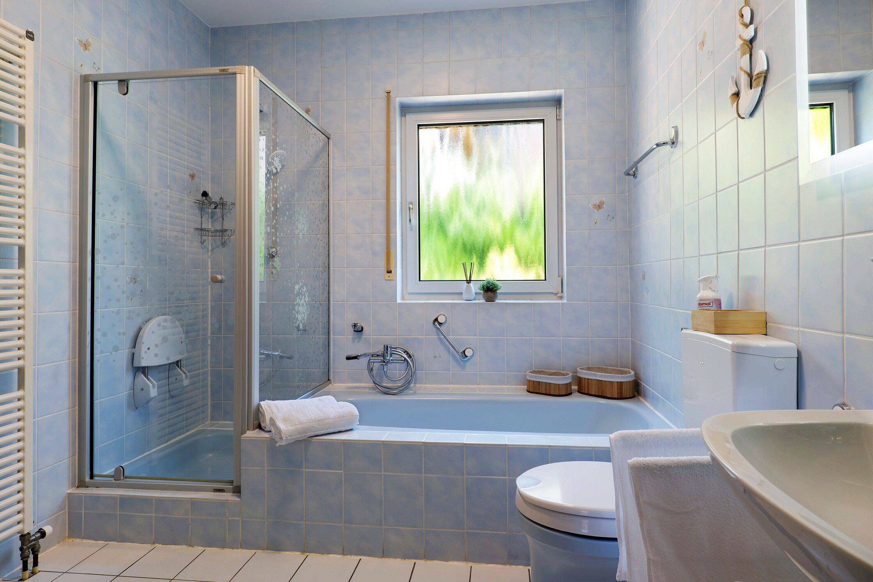 Un bagno con cabina doccia in vetro, vasca da bagno, WC e finestra con vista sul verde.
