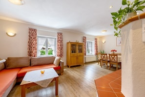 A living room with a sofa, a table, a wooden cabinet, and a dining area with chairs and a table. - Holiday Home 'Becker' with Private Terrace, Private Garden and Wi-Fi (Schönau (Pfalz))