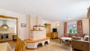 Een woonkamer met een bank, een houten zitbank, een televisie en een raam met gordijnen.