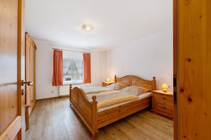A wooden bed in a room with a window, a nightstand, and a door. - Holiday Home 'Becker' with Private Terrace, Private Garden and Wi-Fi (Schönau (Pfalz))