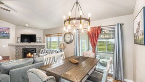 A spacious living room with a fireplace, a dining table, and a large window with curtains. - Ayu Ranch | Panoramic views | Hot tub (Cheyenne)