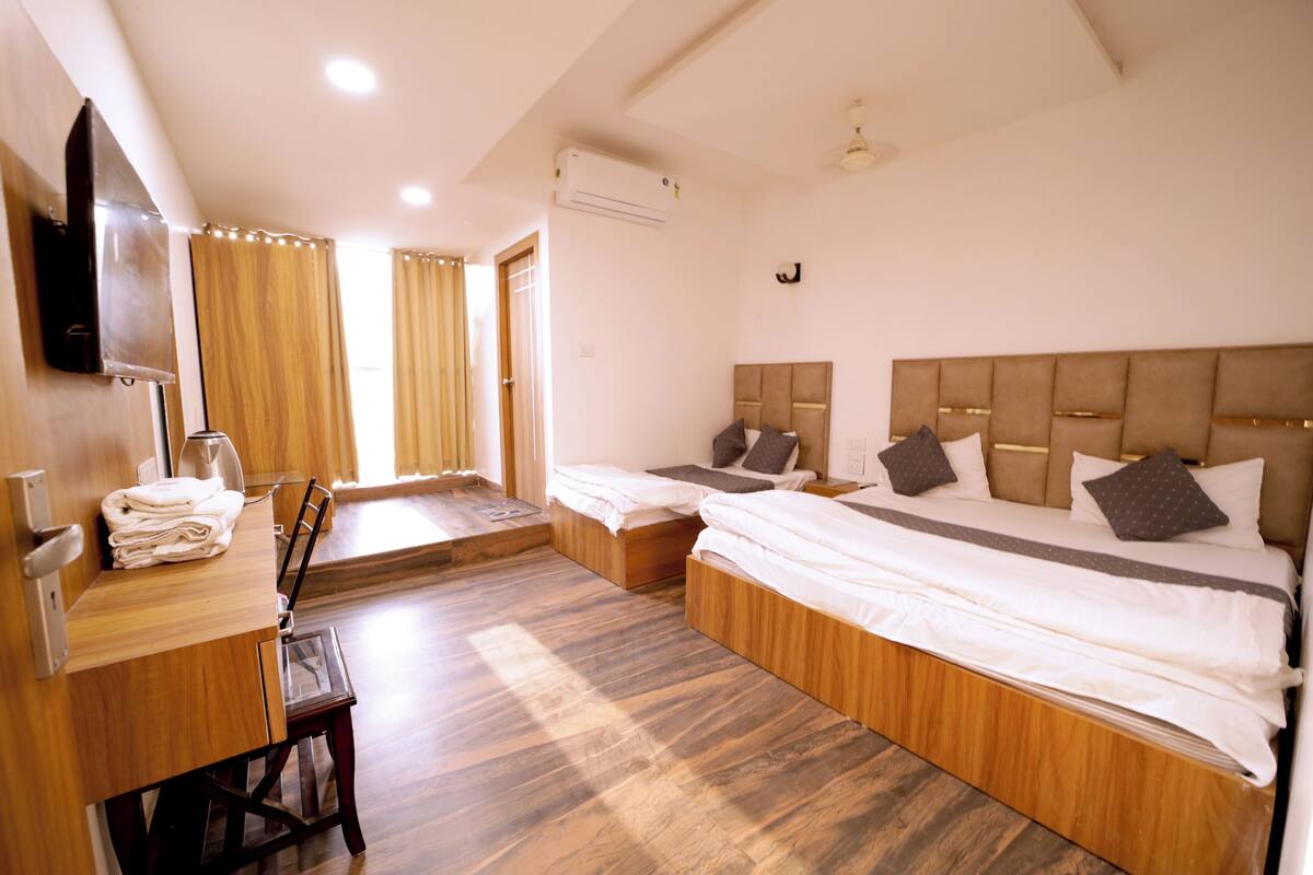 A hotel room with two beds, a wooden desk, a flat-screen TV, and a window with curtains.