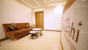 Un hall de hotel con un sofá marrón, dos mesitas redondas y una puerta de madera con el número 312.