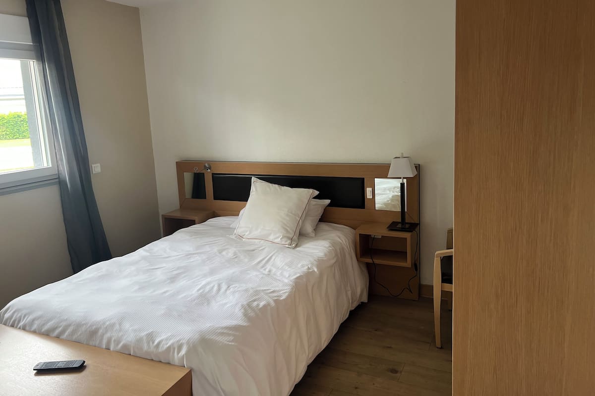 Un lit bien fait, avec du linge de lit blanc, une table de chevet avec une lampe et une tête de lit en bois.