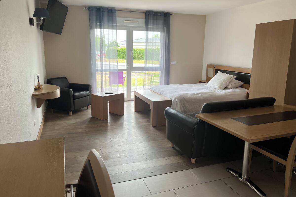 Une chambre d’hôtel moderne équipée d’un lit, d’un bureau, d’une chaise, d’un canapé et d’un téléviseur fixé au mur.