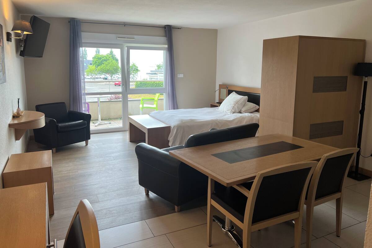 Une chambre d’hôtel comprenant un lit, un bureau, une chaise, un canapé et une armoire. Il y a une fenêtre avec des rideaux et une vue sur l’extérieur.