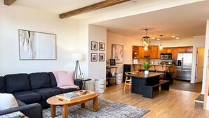 A modern living room with a sofa, coffee table, and a rug. There is a kitchen area with wooden cabinets and a refrigerator. - Ski-In/Out Mountain Escape with Hot Tub (Kimberley)