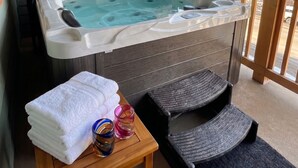 A hot tub in a room with a wooden ceiling, a wooden table with towels and glasses, and a view of trees and mountains outside. - Ski-In/Out Mountain Escape with Hot Tub (Kimberley)