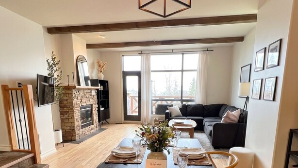 A dining area with a black table set for six, a fireplace, and a living room in the background. - Ski-In/Out Mountain Escape with Hot Tub (Kimberley)