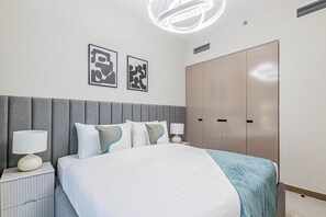 Una habitación de hotel moderna con una cama grande, una mesita de noche con lámpara, un armario y dos obras de arte abstractas en la pared.