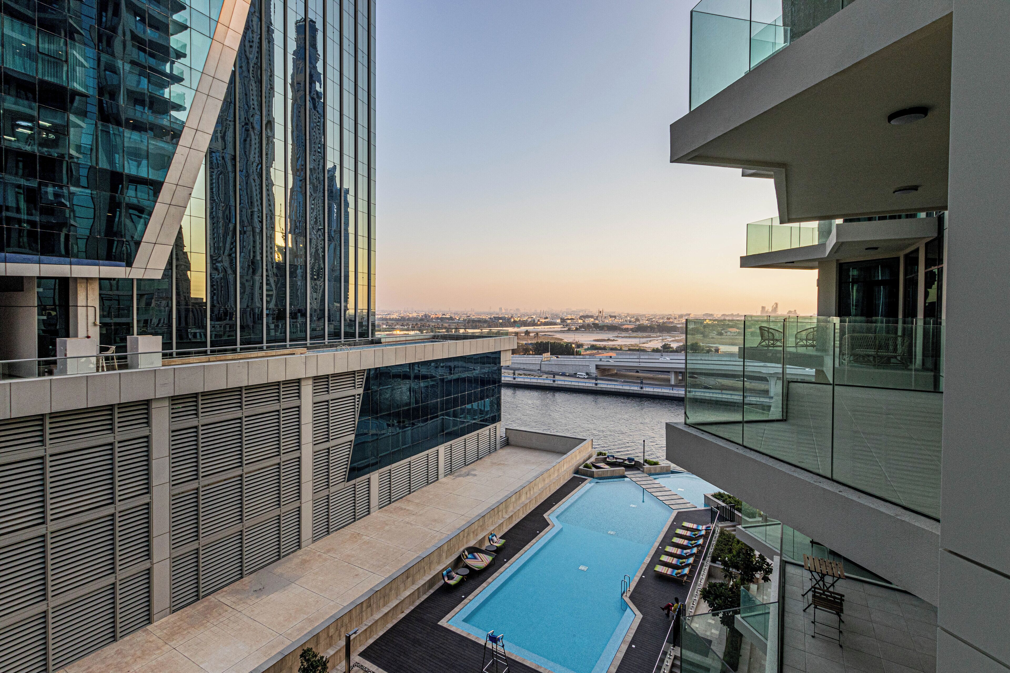 A modern building with a rooftop pool, glass railings, and a view of a cityscape.