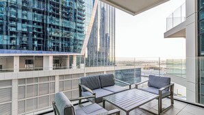 Ein moderner Balkon mit Glasgeländer, einer Couch und einem Tisch, mit Blick auf eine Skyline mit Hochhäusern.