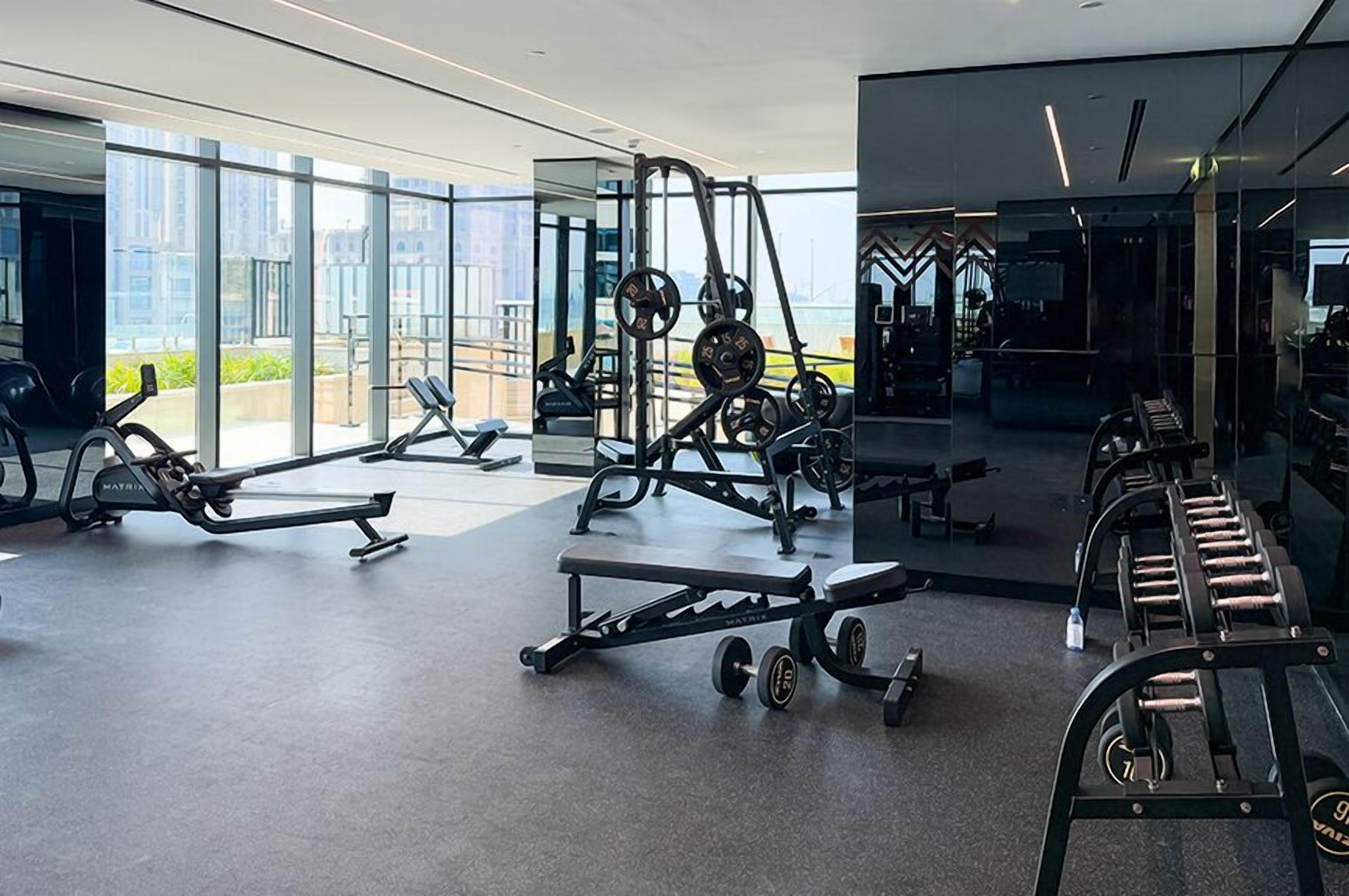A modern gym with various exercise equipment, large windows, and a clean, spacious layout.
