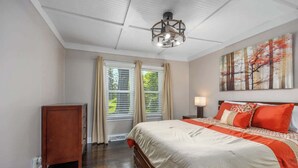 A bedroom with a large bed, a wooden nightstand, a ceiling light fixture, and a window with curtains. - Bluestar Cottage - Hot Tub, Pergola, and Fire pit! (Saugatuck)