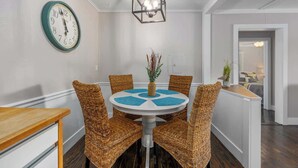 A dining area with a round table, wicker chairs, a clock, and a hanging light fixture. - Bluestar Cottage - Hot Tub, Pergola, and Fire pit! (Saugatuck)