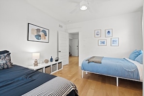 Ein Schlafzimmer mit zwei Betten, einem weißen Deckenventilator und einer Tür zu einem weiteren Raum.