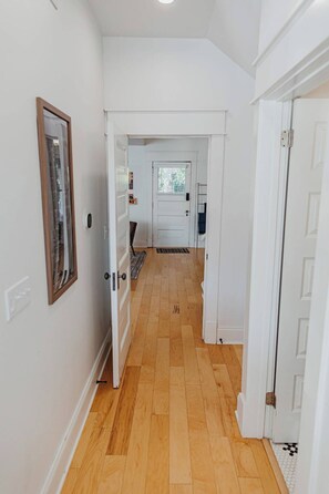 Un couloir doté d’un plancher en bois, de murs blancs et d’une porte donnant sur une pièce avec une fenêtre.