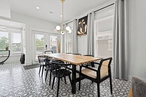 Un comedor con una mesa de madera y sillas negras, una lámpara colgante y un piso con estampado geométrico.