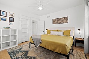 Ein Schlafzimmer mit einem Bett, einem Deckenventilator, einem Nachttisch und einer Wandlampe.