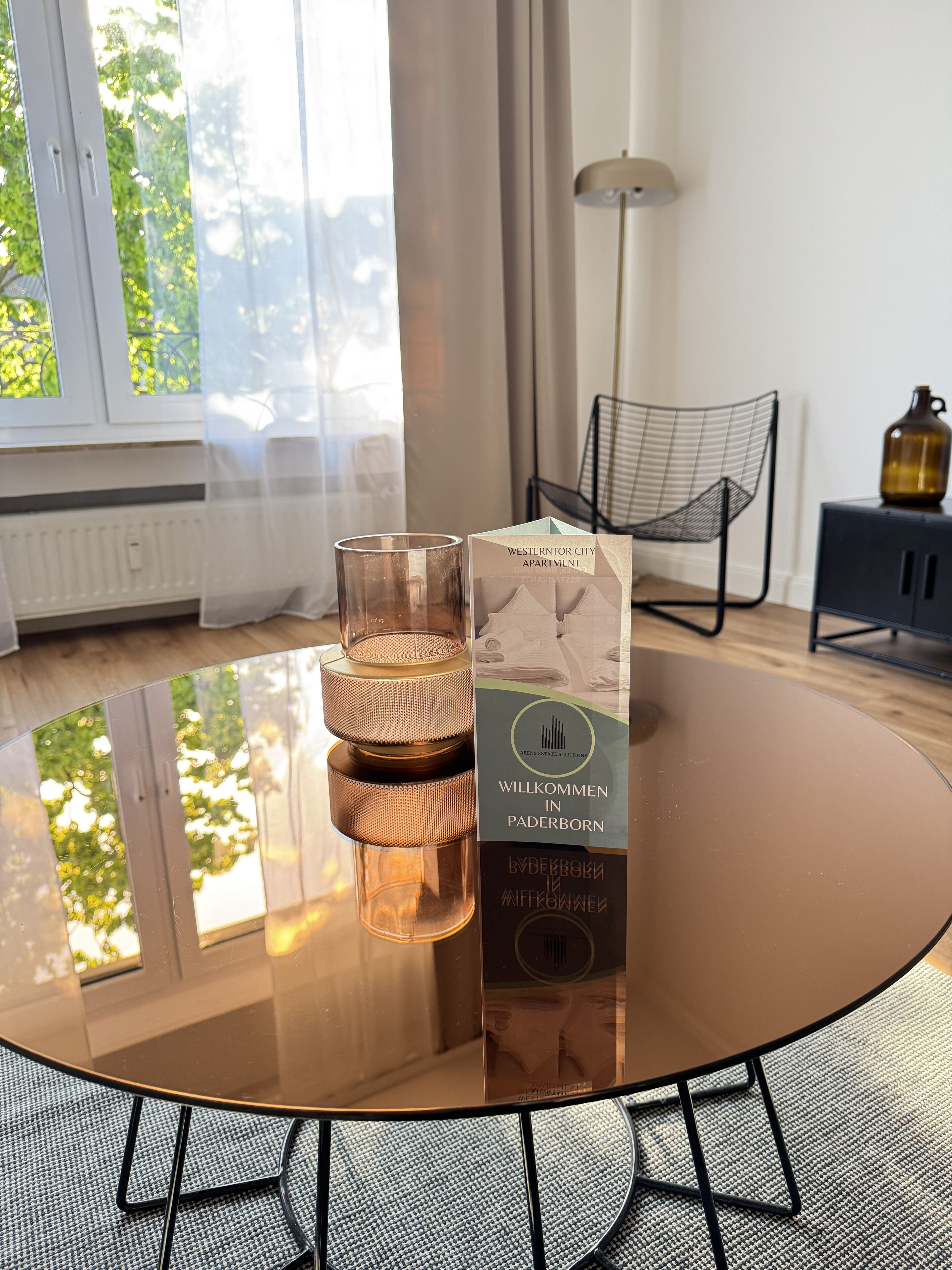 Ein stilvolles Wohnzimmer mit Glastisch, Kerze, Sessel und Lampe.
