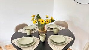 Une table de salle à manger ronde, sur laquelle est posé un vase rempli de fleurs jaunes, entourée de chaises et d’assiettes.