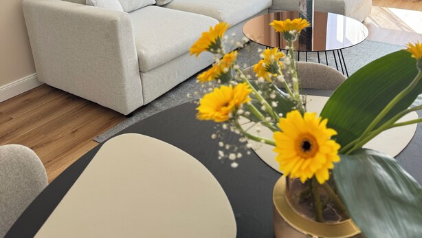 Un salon moderne avec un canapé gris, une table basse ronde et un vase rempli de fleurs jaunes.