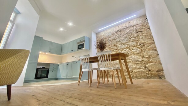A modern kitchen with light blue cabinets, a stone accent wall, and a dining area with wooden chairs and a table.