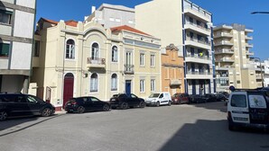 A street with multi-story buildings, parked cars, and a clear blue sky.