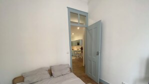 A bedroom with a bed, a door leading to a kitchen, and a small sitting area.