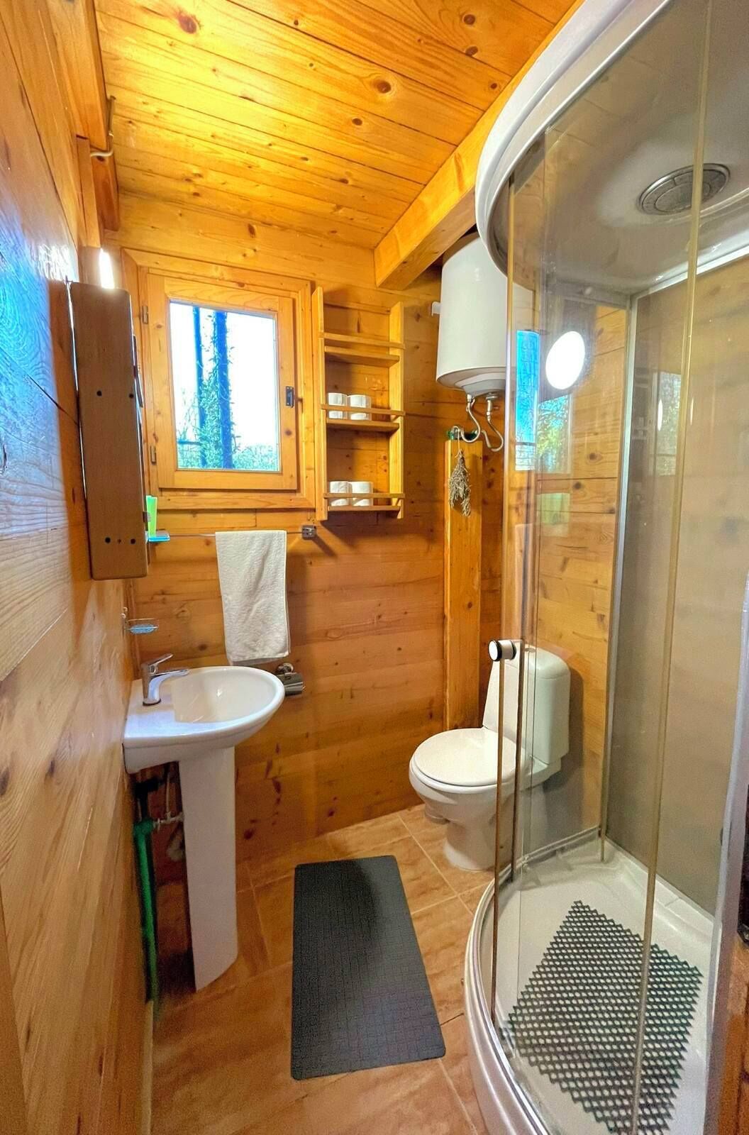 Baño de cabaña de madera con lavamanos, inodoro y mampara de vidrio para la ducha.