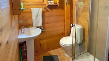 Baño de cabaña de madera con lavamanos, inodoro y mampara de vidrio para la ducha.