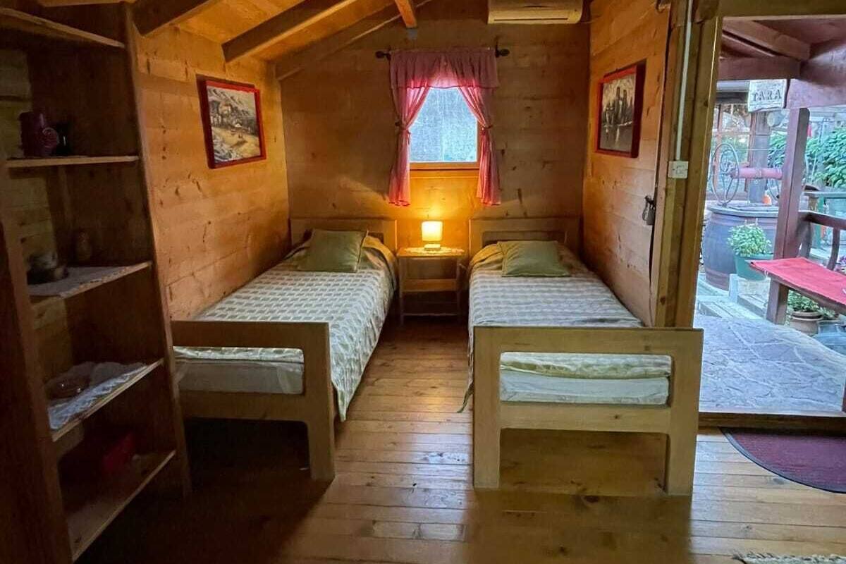 A cozy cabin with two wooden beds, a small window with curtains, and a wooden ceiling.