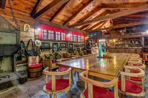 A rustic wooden interior with a long communal table, red cushioned chairs, and a bar area with shelves of bottles. - Eco Houses Drvljanik Buljarica (Petrovac)
