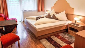 A hotel room with a bed, a desk, a chair, a nightstand, and a window with curtains.