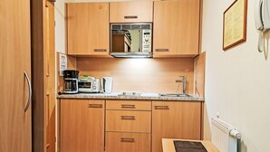 A compact kitchenette with wooden cabinets, a built-in microwave, a coffee maker, and a small table with a black object on it.