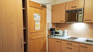 A compact kitchen with wooden cabinets, a stainless steel microwave, a coffee maker, a toaster, and a sink.