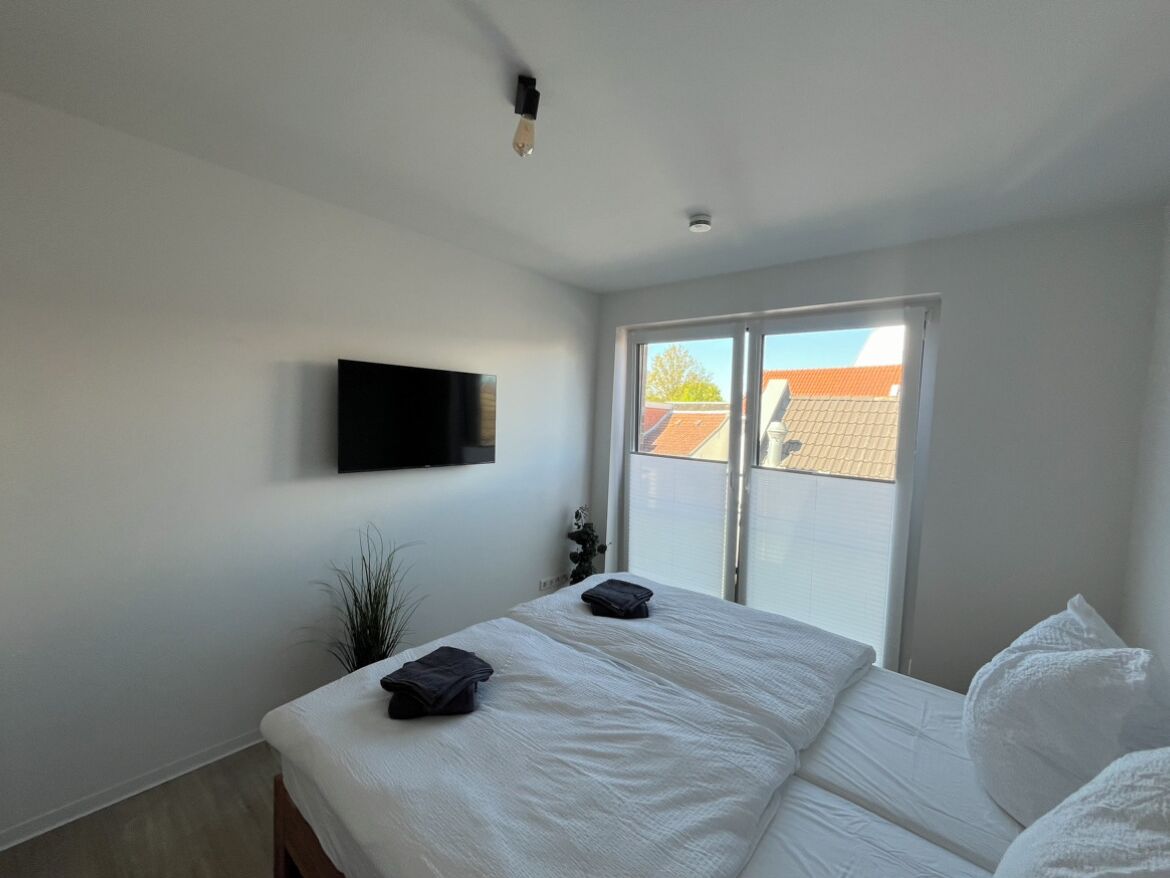 Un dormitorio con cama, un televisor de pantalla plana montado en la pared y un ventanal corredizo que da a un espacio exterior.